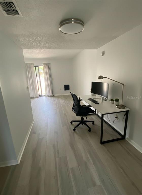 A home office area features light-colored wood-look flooring, a desk with a monitor, and sliding doors — 22707 WATERSEDGE BOULEVARD UNIT 57, LAND O LAKES, FL
