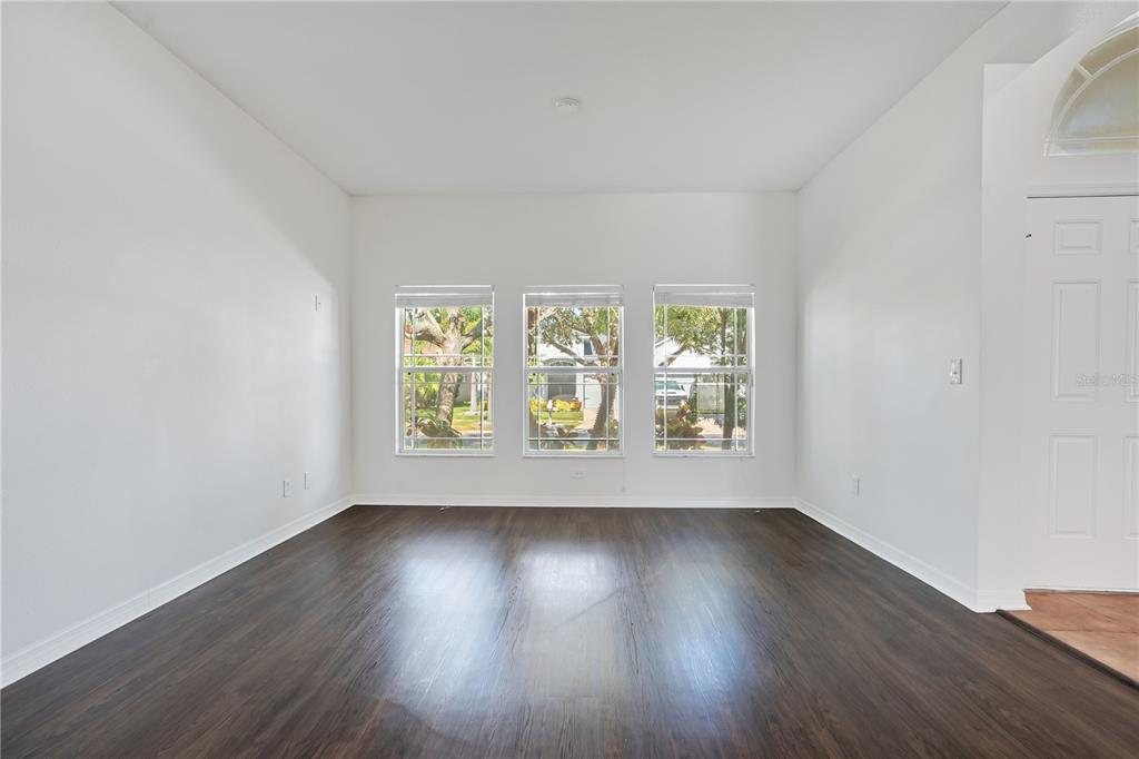 An empty room features white walls, dark wood-look flooring, and three windows overlooking trees — 432 YORK DALE DRIVE, RUSKIN, FL