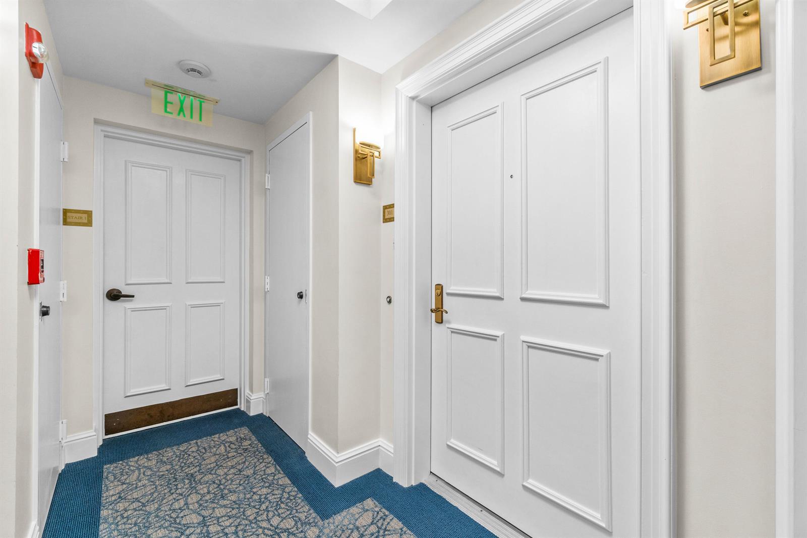 A hallway with blue patterned carpet, white doors, and gold wall sconces — 340 S Us Hwy 1 # 301, Jupiter FL 33477, JUPITER, FL