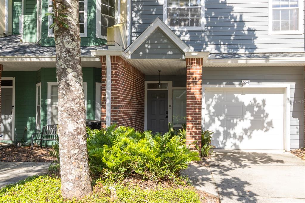 A two-story townhouse exterior features a brick-accented entryway, a garage, and green siding — 5047 NW 1ST PLACE UNIT 92, GAINESVILLE, FL