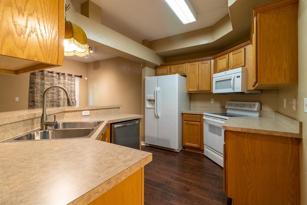 A kitchen with oak cabinets, white appliances, laminate countertops, and dark wood-look flooring — 5047 NW 1ST PLACE UNIT 92, GAINESVILLE, FL