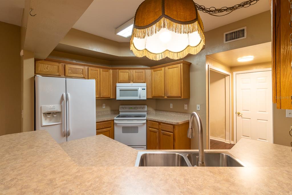 A kitchen features oak cabinets, white appliances, laminate countertops, and a large hanging pendant light — 5047 NW 1ST PLACE UNIT 92, GAINESVILLE, FL