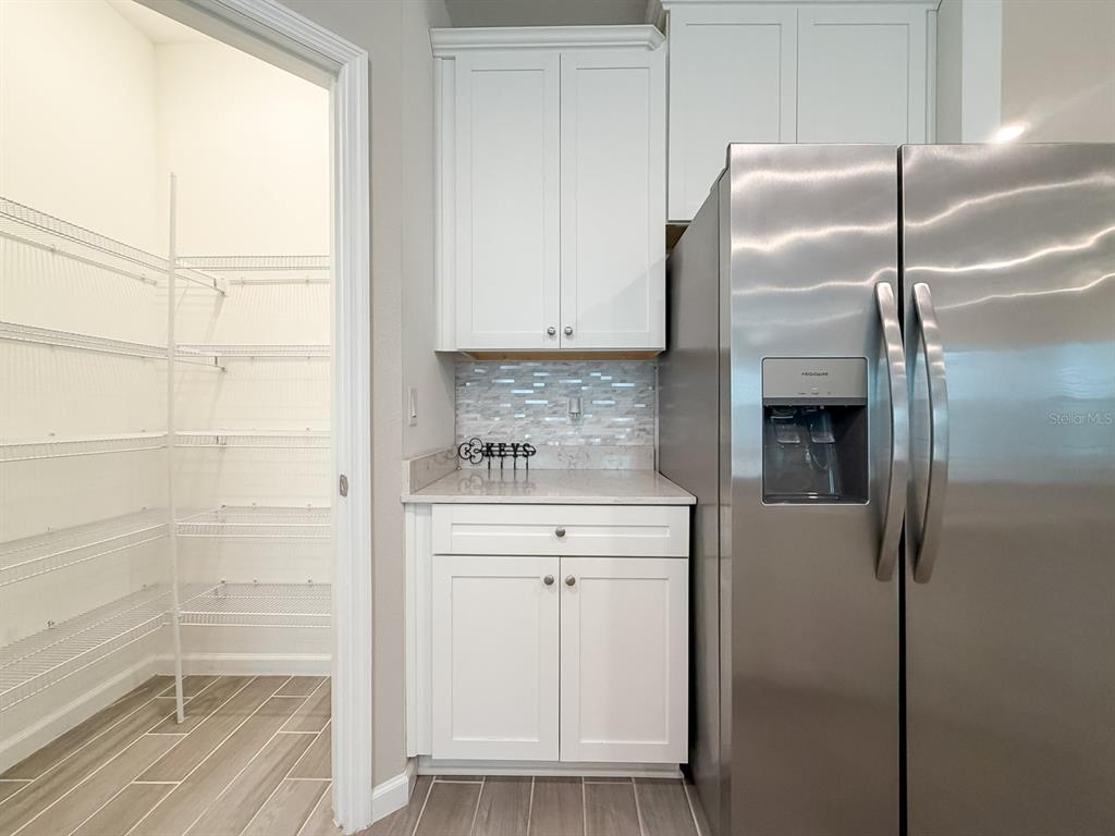 A kitchen area features white cabinets, a stainless steel refrigerator, and an adjacent walk-in pantry — 2258 NW 89TH WAY, GAINESVILLE, FL