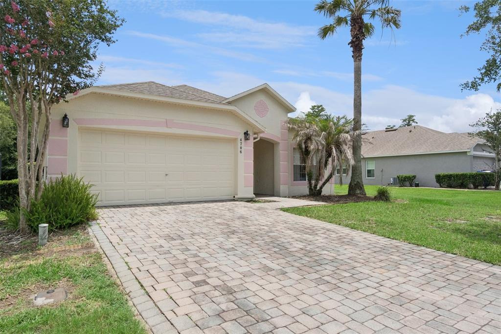 A single-story house with a paved driveway, a two-car garage, and pink exterior trim — 4706 CUMBRIAN LAKES DRIVE, KISSIMMEE, FL