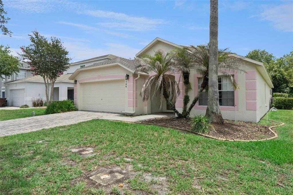 A single-story house with a two-car garage, pink trim, and a palm tree in front — 4706 CUMBRIAN LAKES DRIVE, KISSIMMEE, FL