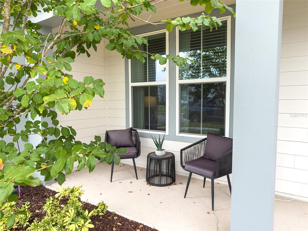 A small covered porch features two dark chairs and a side table near a window — 5640 PINELAND RUN, ORLANDO, FL