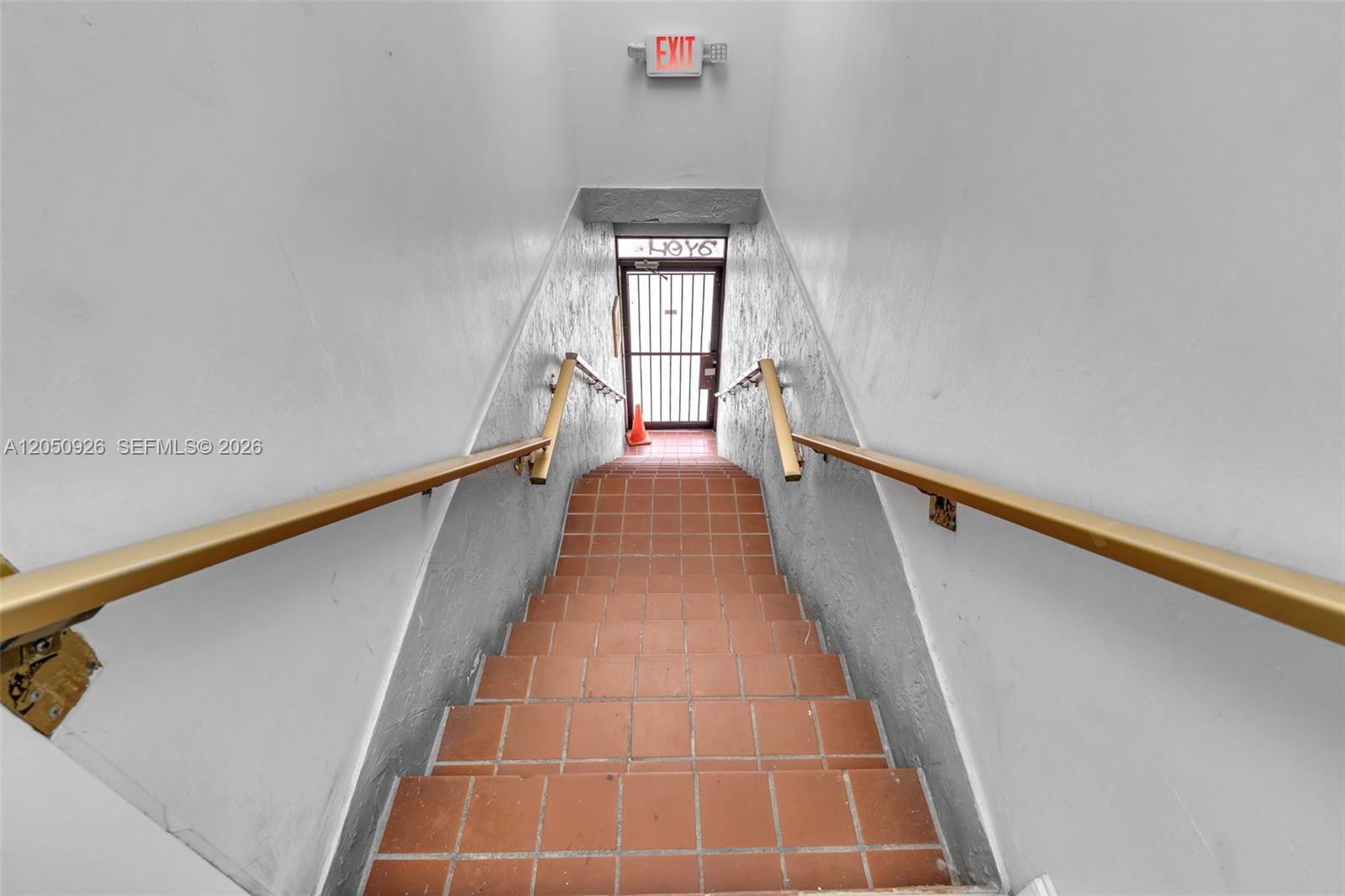 A downward view of a tiled staircase with handrails leading to an exterior security door — 1879 NW 7th St # 2, Miami FL 33125, MIAMI, FL