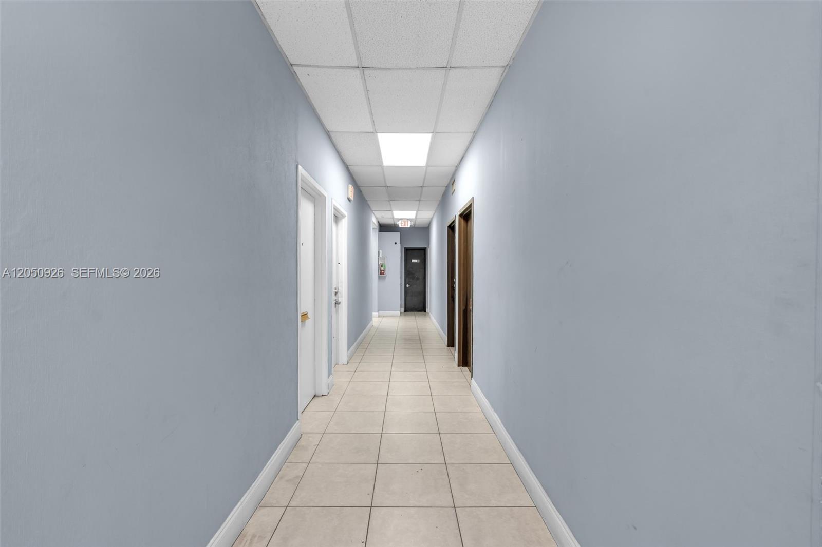 A long, narrow hallway features light blue walls, a drop ceiling, and beige tiled flooring — 1879 NW 7th St # 2, Miami FL 33125, MIAMI, FL
