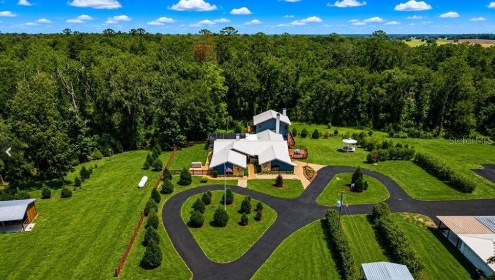 An aerial view shows a house with a metal roof surrounded by a large lawn — 27255 HICKORY HILL ROAD, BROOKSVILLE, FL