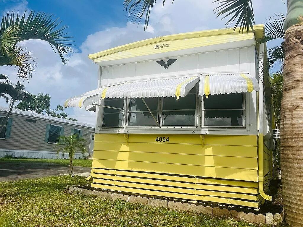 A yellow mobile home with a white metal awning and a decorative bird emblem — 4054 Marigold Road, Boynton Beach FL 33436, BOYNTON BEACH, FL