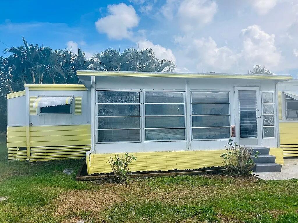 A yellow and white mobile home features a large screened-in porch with jalousie windows — 4054 Marigold Road, Boynton Beach FL 33436, BOYNTON BEACH, FL