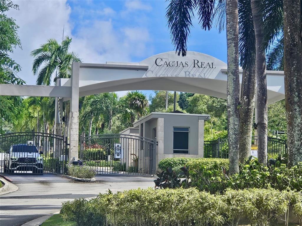 The gated entrance to Caguas Real features a white archway, security booth, and palm trees — H 11 CAGUAS REAL, TORRES DEL ORO, CAGUAS, PR