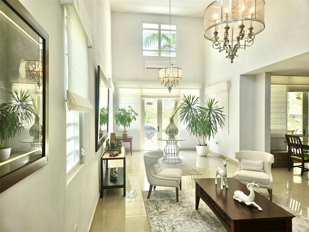 A bright, high-ceilinged living room features white walls, tile floors, two chandeliers, and large windows — H 11 CAGUAS REAL, TORRES DEL ORO, CAGUAS, PR