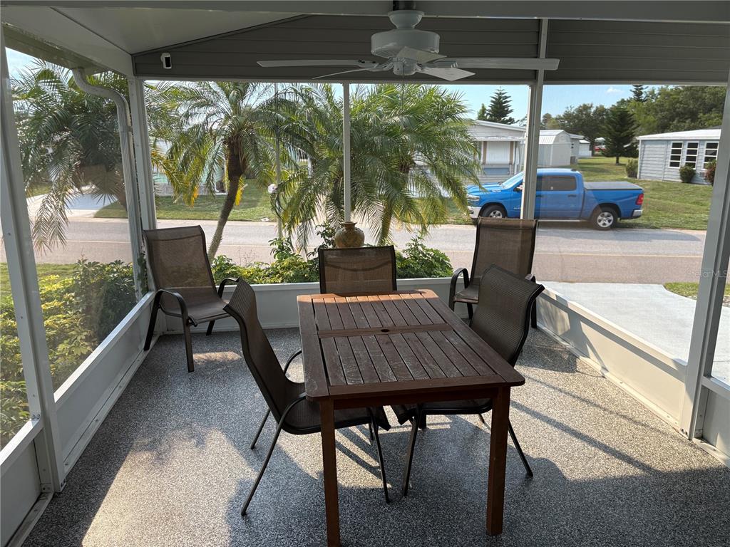 A screened-in porch features a wooden dining set, a ceiling fan, and a view outside — 5696 HOLIDAY PARK BOULEVARD, NORTH PORT, FL