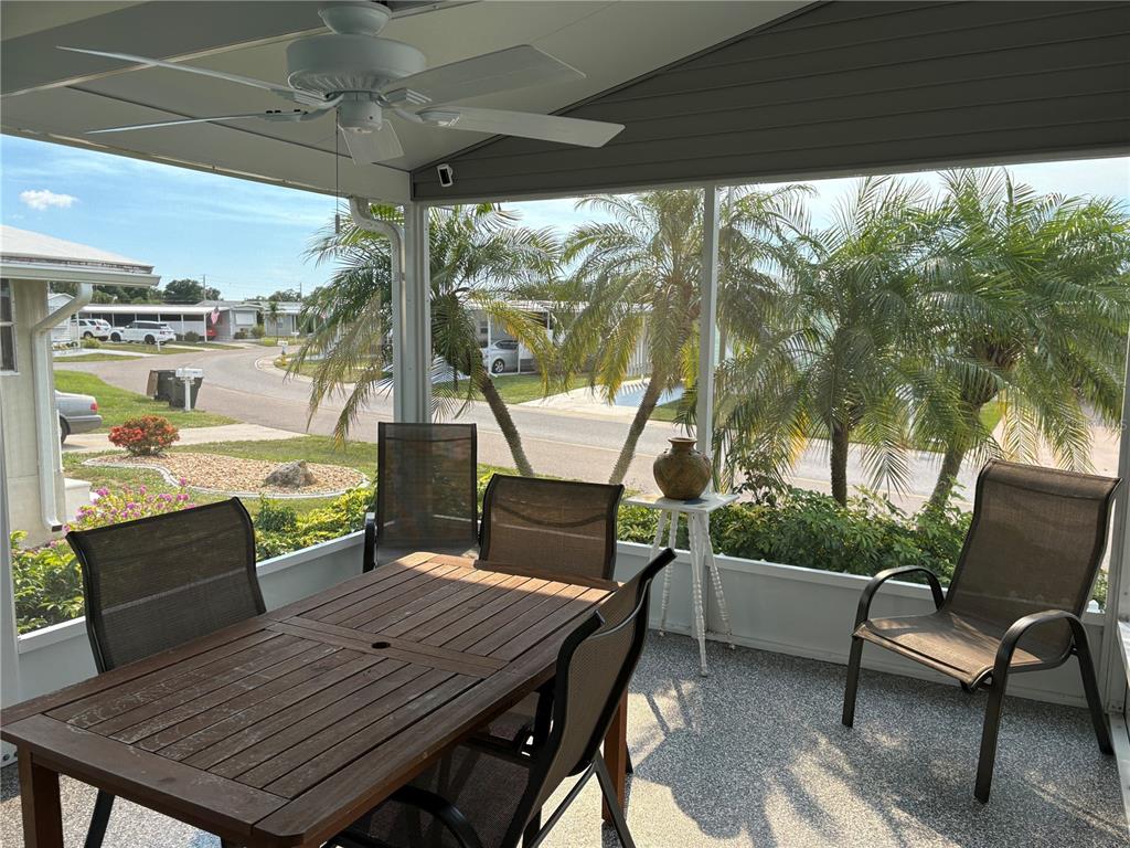 A screened-in porch features a wooden dining set, a ceiling fan, and palm tree views — 5696 HOLIDAY PARK BOULEVARD, NORTH PORT, FL