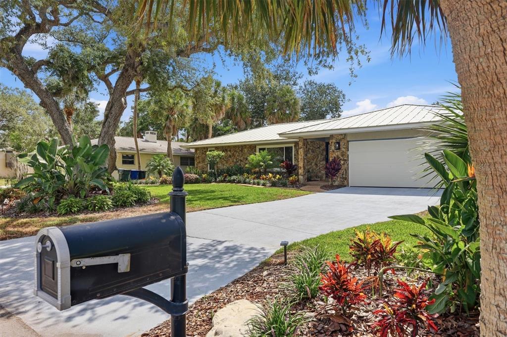 A single-story house with a stone facade, metal roof, and driveway viewed from the street — 5159 OAKMONT PLACE, SARASOTA, FL