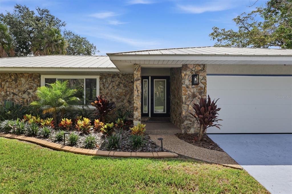A single-story house features a stone facade, a metal roof, and a landscaped front yard — 5159 OAKMONT PLACE, SARASOTA, FL