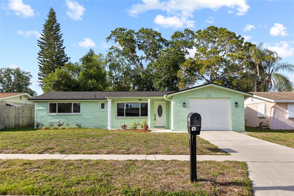 A single-story house with light green stone siding, a white garage door, and a mailbox — 6239 7TH AVENUE, NEW PORT RICHEY, FL
