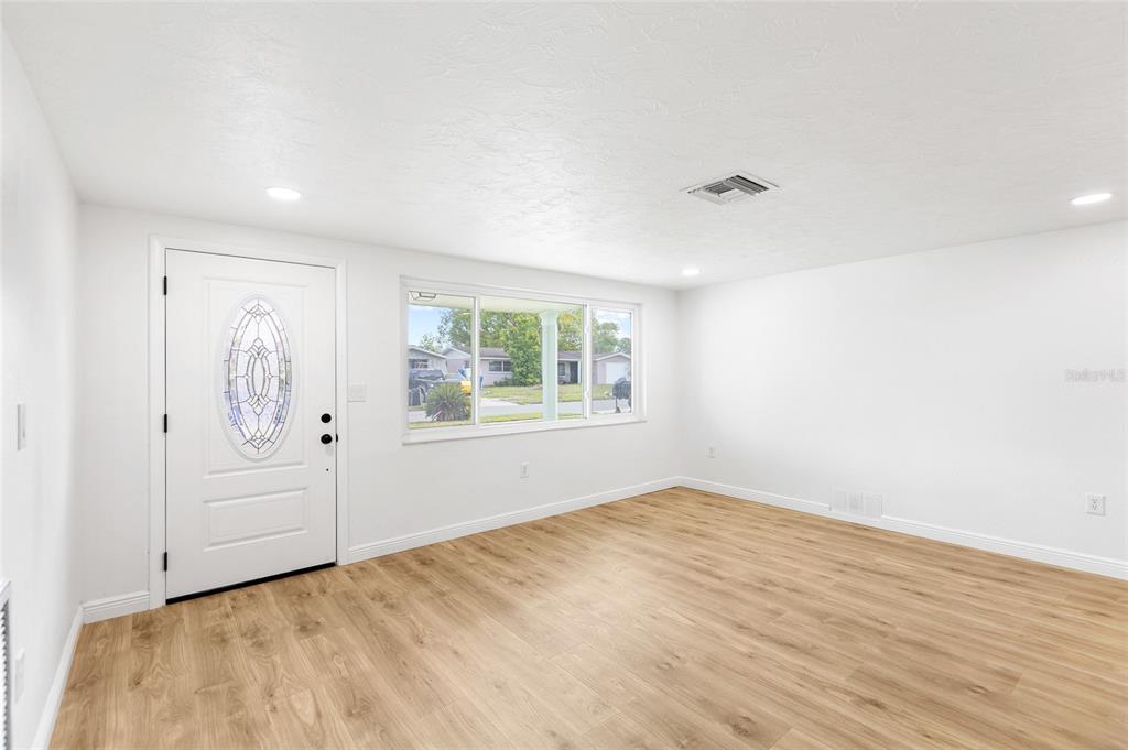 An empty room with white walls, light wood-look flooring, a front door, and a window — 6239 7TH AVENUE, NEW PORT RICHEY, FL