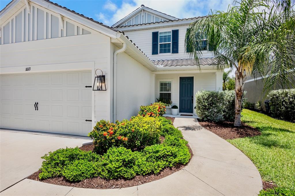 A two-story white house features a garage, a front walkway, and landscaped bushes — 10113 CANAVERAL CIRCLE, SARASOTA, FL