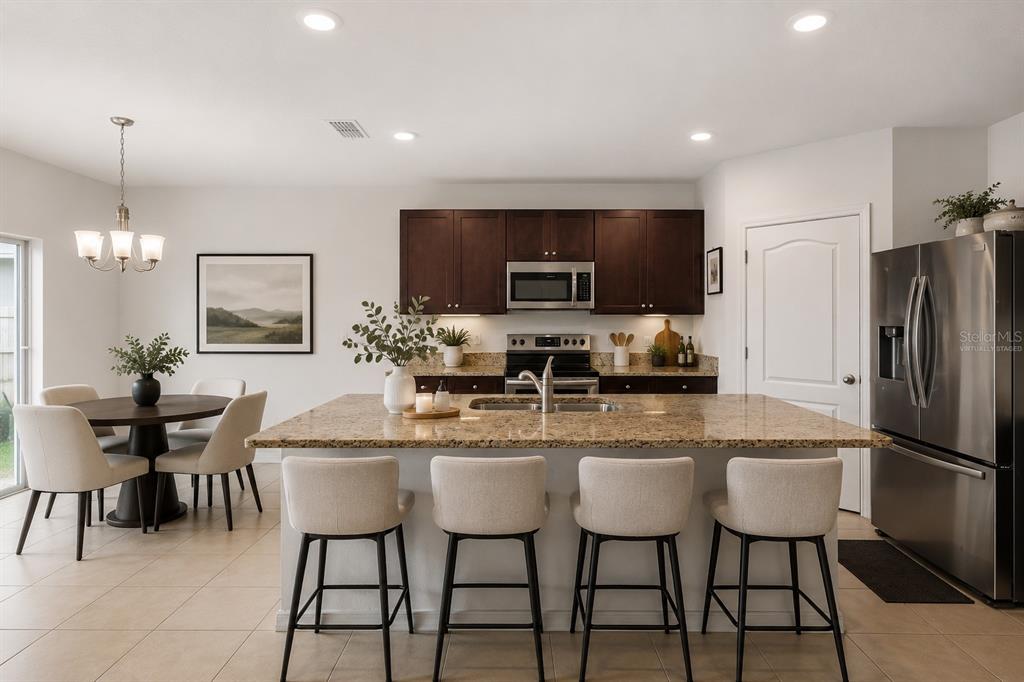 A kitchen features dark wood cabinets, granite countertops, a central island, and a dining area — 5125 FIDDLEWOOD WAY, ST CLOUD, FL