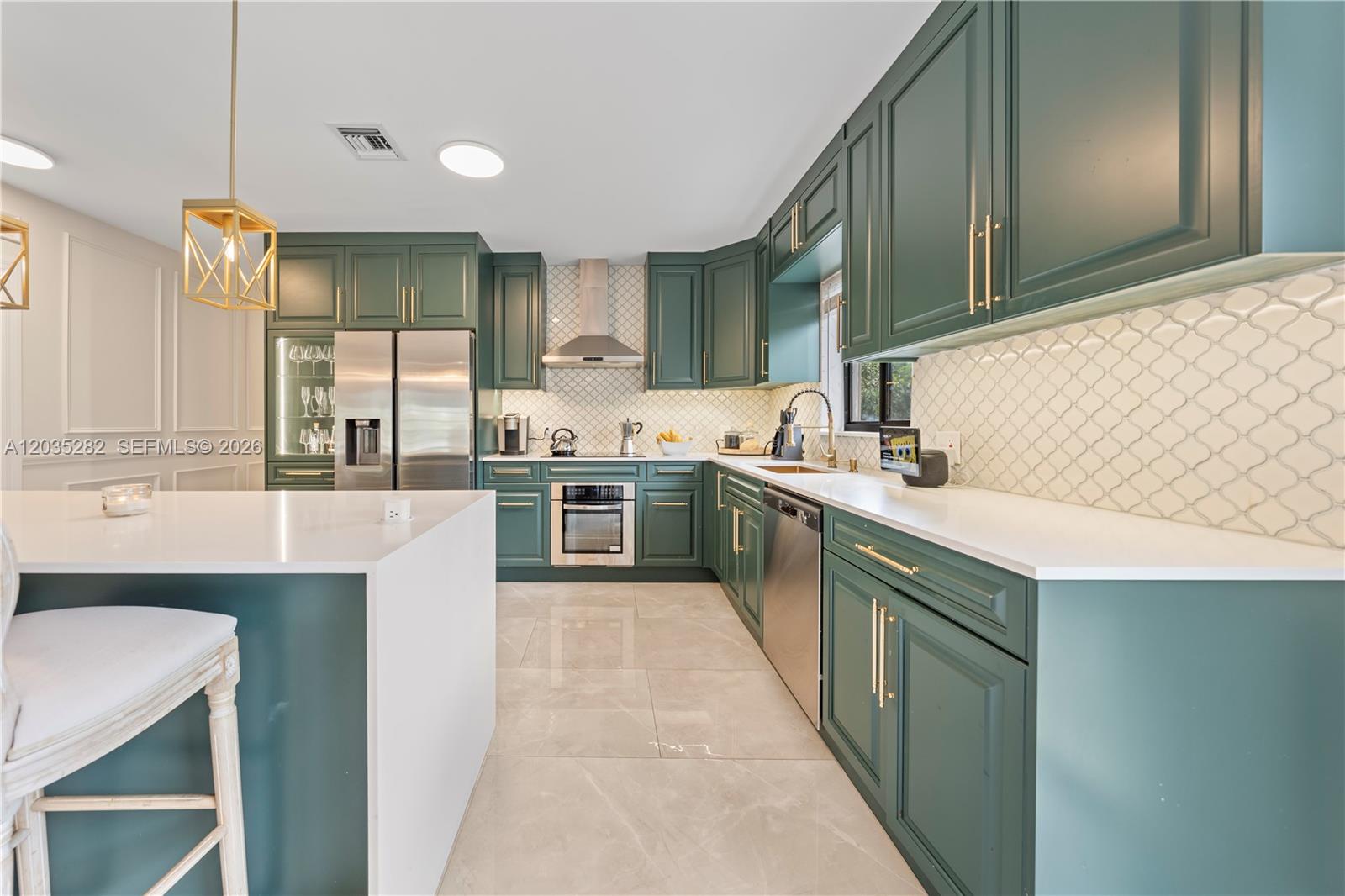 A kitchen features dark green cabinets, white countertops, a tiled backsplash, and a central island — 1302 Fillmore St, Hollywood FL 33019, HOLLYWOOD, FL