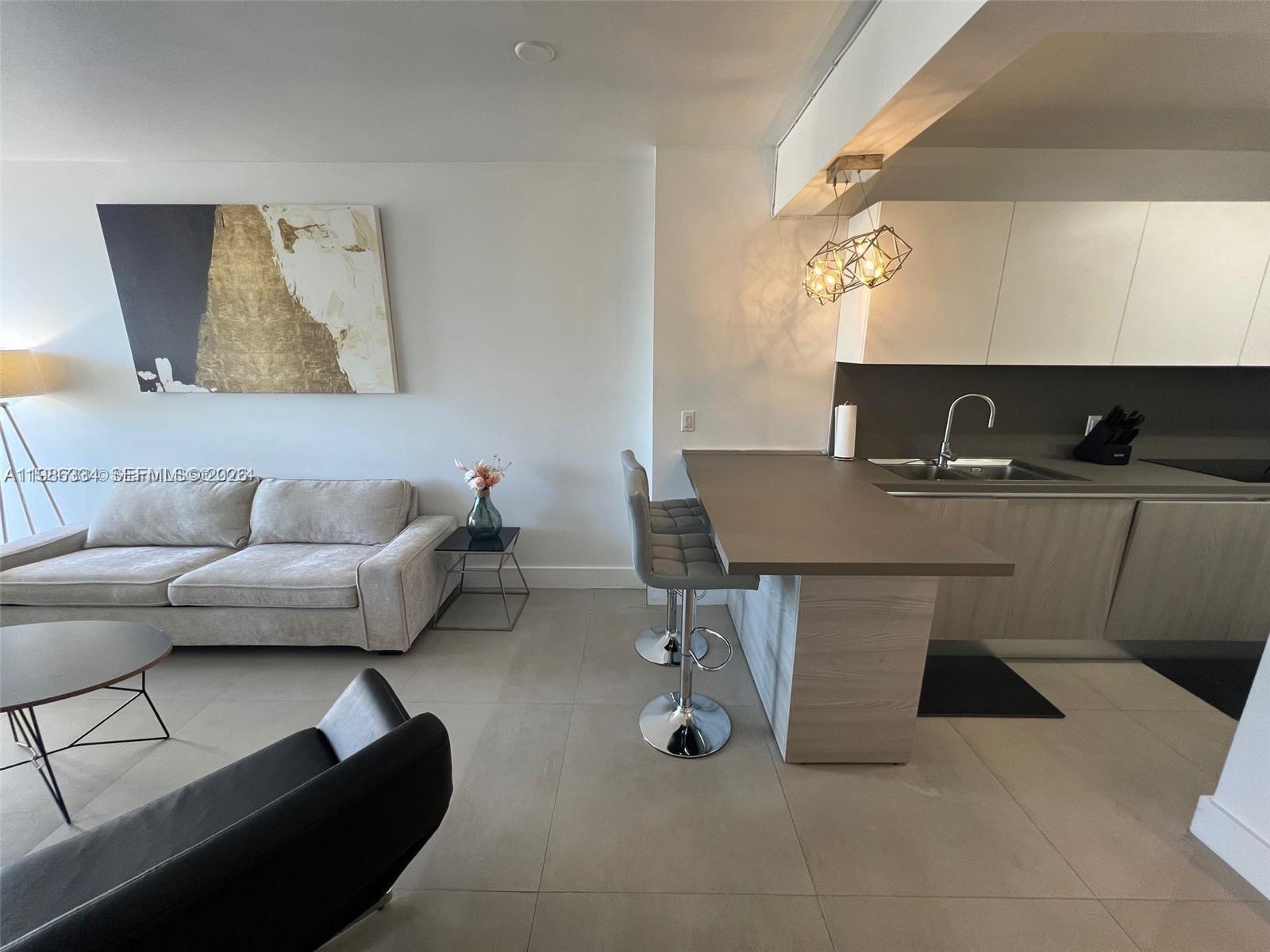 A modern living room features a sofa, a kitchen island with bar stools, and artwork — 100 Lincoln Rd # 620, Miami Beach FL 33139, MIAMI BEACH, FL