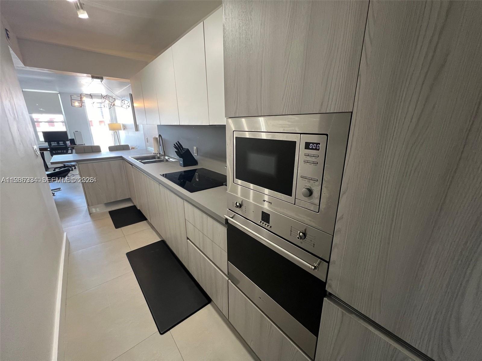 A modern kitchen features light wood cabinetry, stainless steel appliances, and a black cooktop — 100 Lincoln Rd # 620, Miami Beach FL 33139, MIAMI BEACH, FL