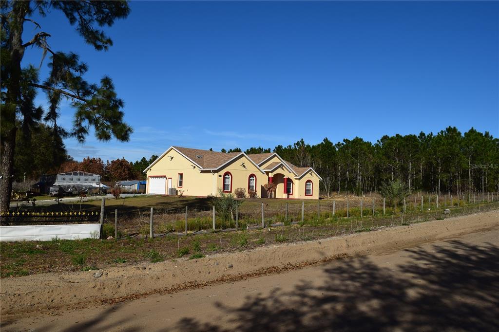 A single-story tan house with a shingled roof sits behind a wire fence — 7901 N CHERRY LAKE GROVES ROAD, GROVELAND, FL