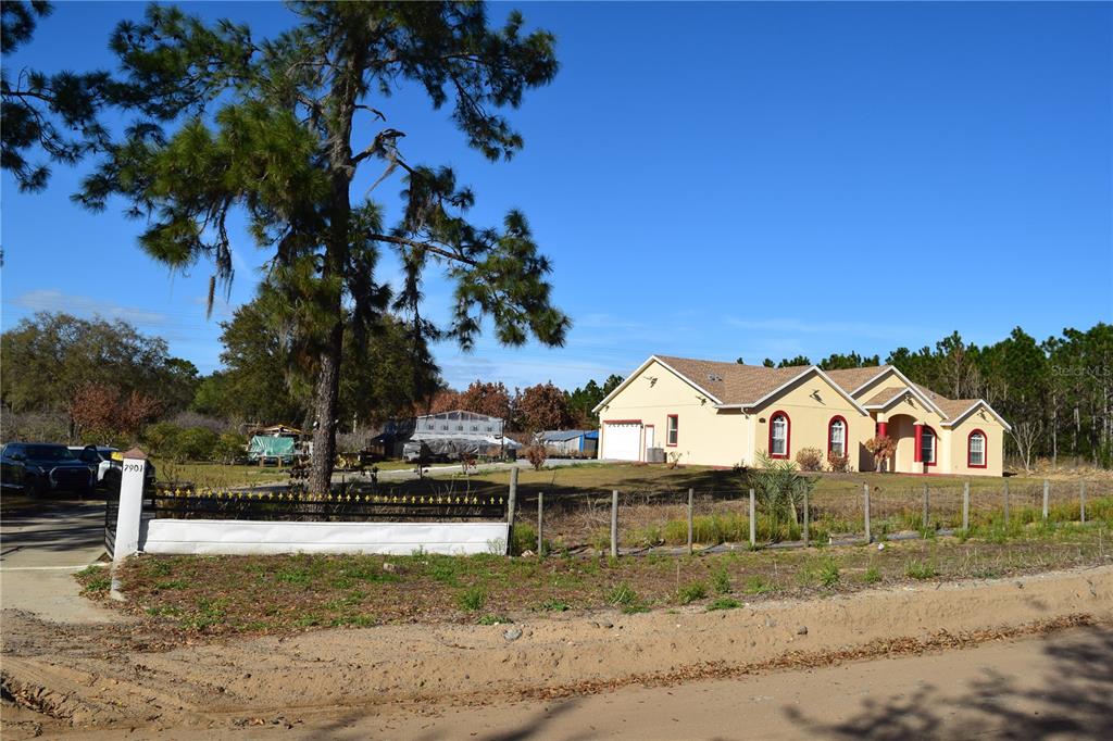 A single-story house with a tan exterior sits behind a fence and a large tree — 7901 N CHERRY LAKE GROVES ROAD, GROVELAND, FL