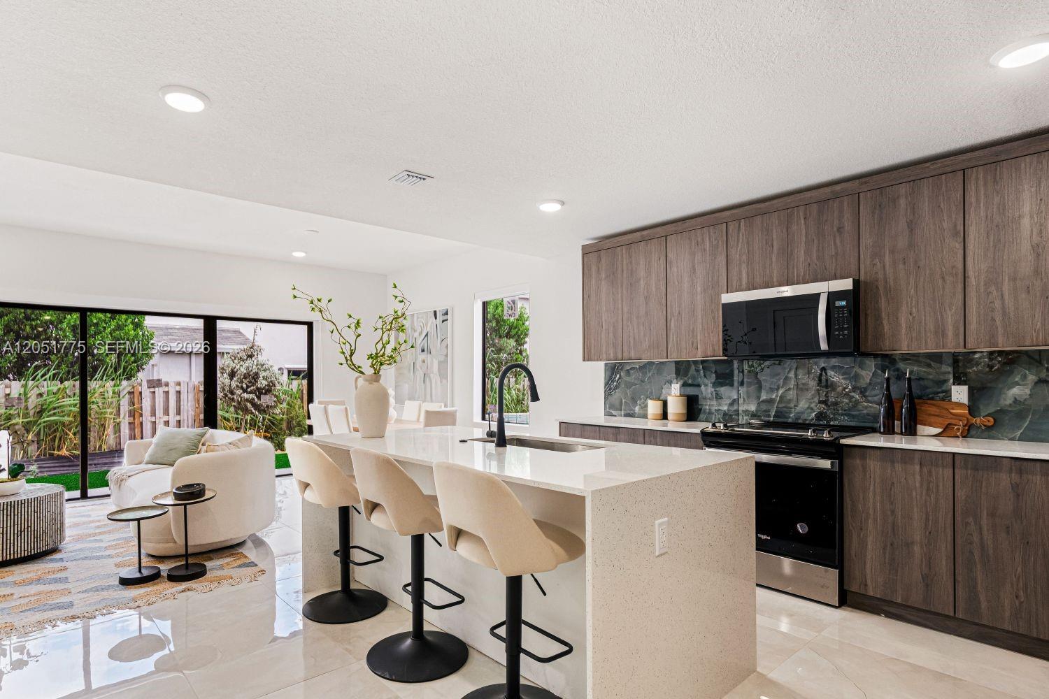 A modern kitchen features dark wood cabinets, a quartz island with bar stools, and a backsplash — 522 NW 14 CT, Florida City FL 33034, FLORIDA CITY, FL