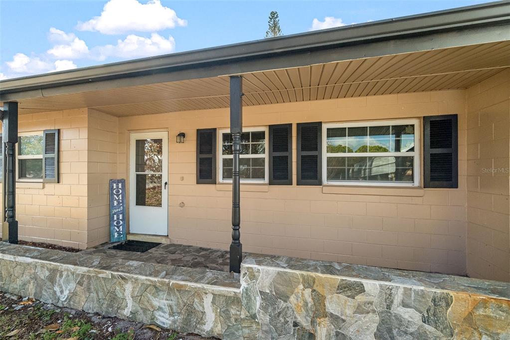 A tan concrete block house features a stone-faced porch, black shutters, and a front door — 1148 N SINGLETON AVENUE, TITUSVILLE, FL