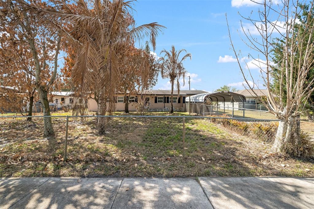 A single-story house with a carport sits behind a chain-link fence and dead trees — 1148 N SINGLETON AVENUE, TITUSVILLE, FL