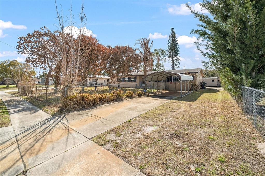 A single-story house with a metal carport, chain-link fencing, and a concrete driveway — 1148 N SINGLETON AVENUE, TITUSVILLE, FL