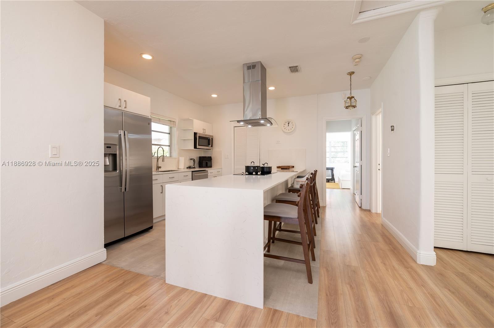 A modern kitchen features a white waterfall island, stainless steel appliances, and light wood flooring — 501 SW 24th Rd # 501, Miami FL 33129, MIAMI, FL