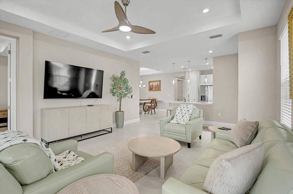 A living room features light-colored furniture, a ceiling fan, and an open-concept kitchen beyond — 7782 WANING MOON WAY, SARASOTA, FL