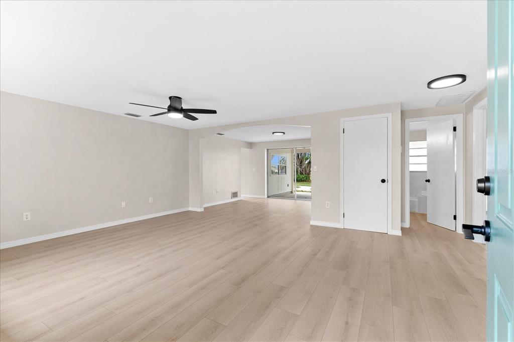 An empty living room features light wood-look flooring, a ceiling fan, and a sliding glass door — 3445 GULF LANE, ROTONDA WEST, FL