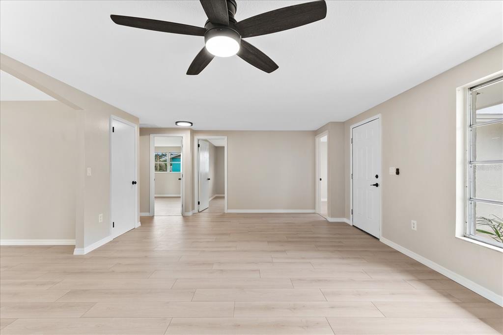 A bright room features light wood-look flooring, beige walls, a ceiling fan, and multiple doorways — 3445 GULF LANE, ROTONDA WEST, FL