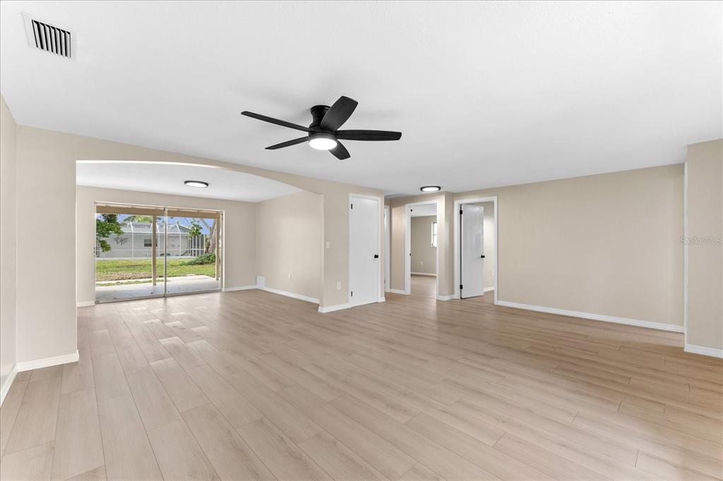 An open-concept living area features light wood-look flooring, a ceiling fan, and sliding glass doors — 3445 GULF LANE, ROTONDA WEST, FL