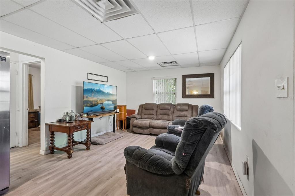 A living room features a drop ceiling, light wood-look flooring, a television, and brown furniture — 2315 EDGEWATER AVENUE, LEESBURG, FL