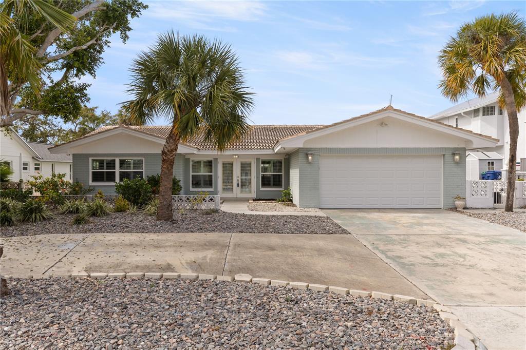 A single-story house with a light blue brick exterior, a two-car garage, and palm trees — 404 4TH AVENUE N, TIERRA VERDE, FL