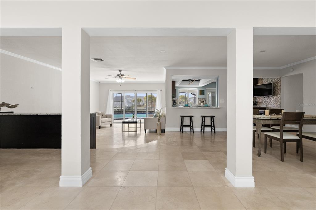 An open-concept living area features tile flooring, a kitchen pass-through, and a view of a pool — 404 4TH AVENUE N, TIERRA VERDE, FL