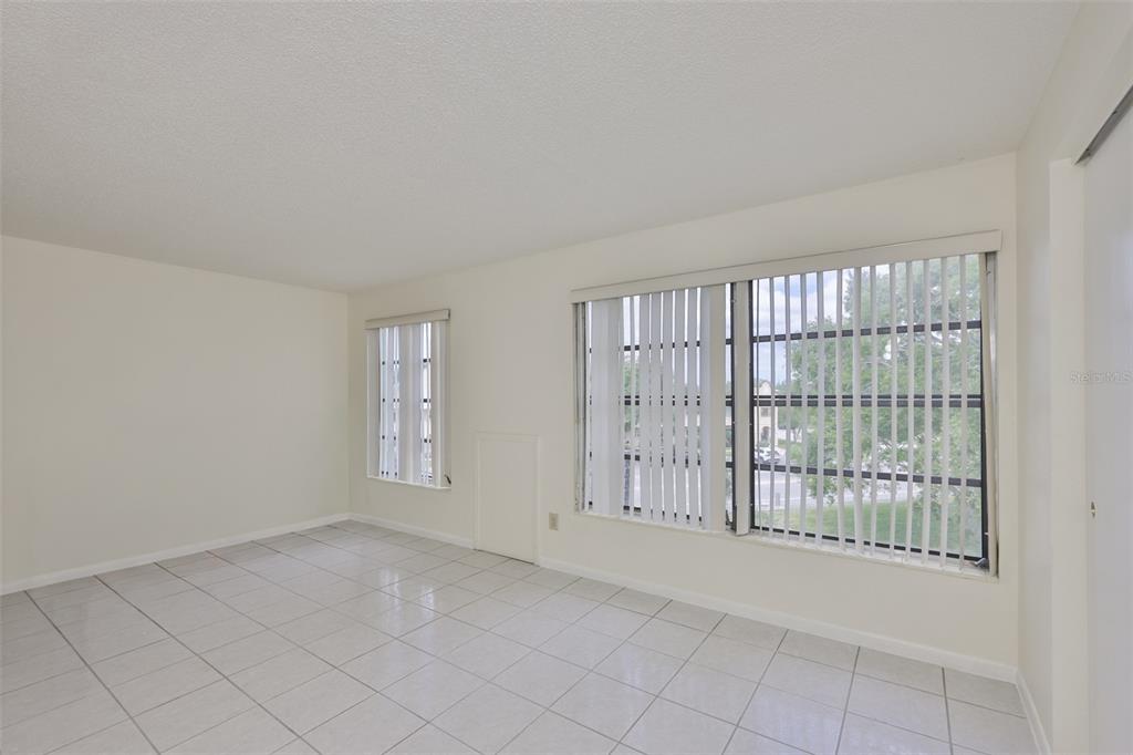A bright, empty room features white tiled floors, off-white walls, and large windows with blinds — 2358 ECUADORIAN WAY UNIT 56, CLEARWATER, FL