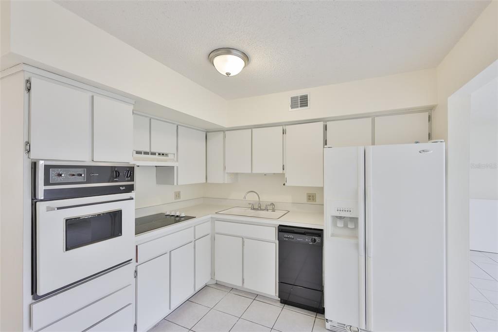 A kitchen features white cabinets, white appliances, a black dishwasher, and white tiled flooring — 2358 ECUADORIAN WAY UNIT 56, CLEARWATER, FL