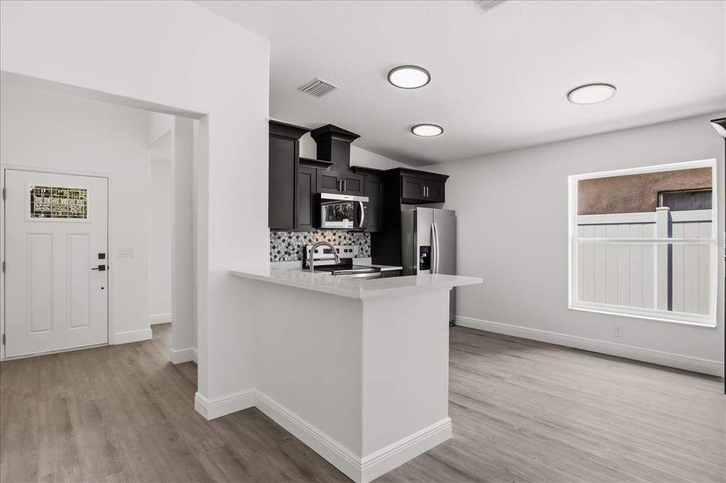 A kitchen with dark cabinets, white countertops, and a breakfast bar overlooks an adjacent room — 710 BEECHER STREET, LEESBURG, FL
