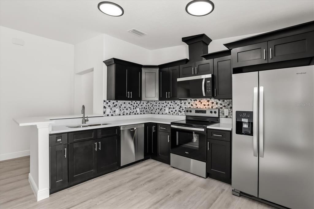 A kitchen features dark cabinets, stainless steel appliances, white countertops, and a patterned tile backsplash — 710 BEECHER STREET, LEESBURG, FL