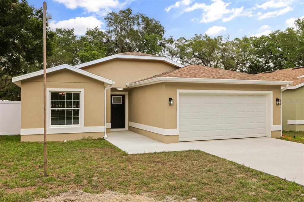A tan, single-story house with a white garage door, black front door, and shingled roof — 710 BEECHER STREET, LEESBURG, FL