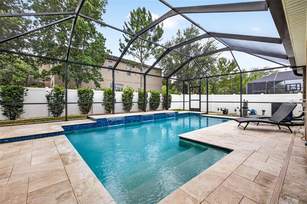 A screened-in swimming pool with a stone deck and water features in a backyard — 29894 CHAPEL CHASE DRIVE, WESLEY CHAPEL, FL