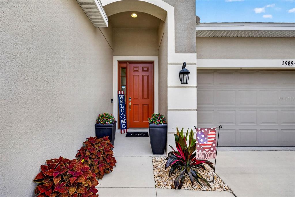 The exterior of a home features a red front door, potted plants, and a garage — 29894 CHAPEL CHASE DRIVE, WESLEY CHAPEL, FL