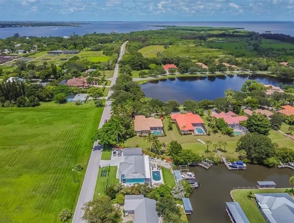 An aerial view shows waterfront homes with pools along a canal near a large lake — 1704 AMBERWYND CIRCLE W, PALMETTO, FL